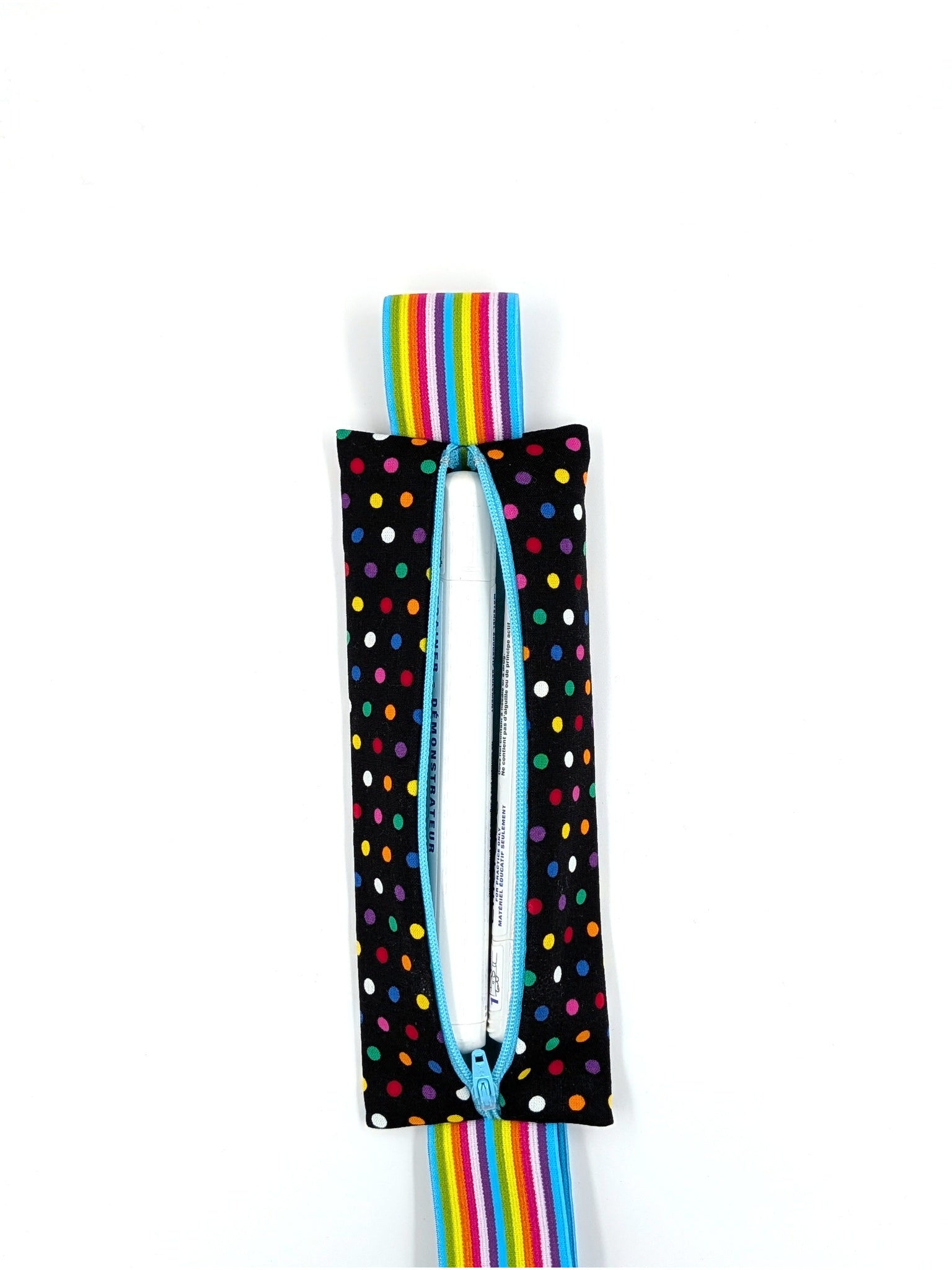 The Daydreamer EpiPen pouch in a black confetti dot print with the rainbow elastic strap, open with an auto-injector trainer inside
